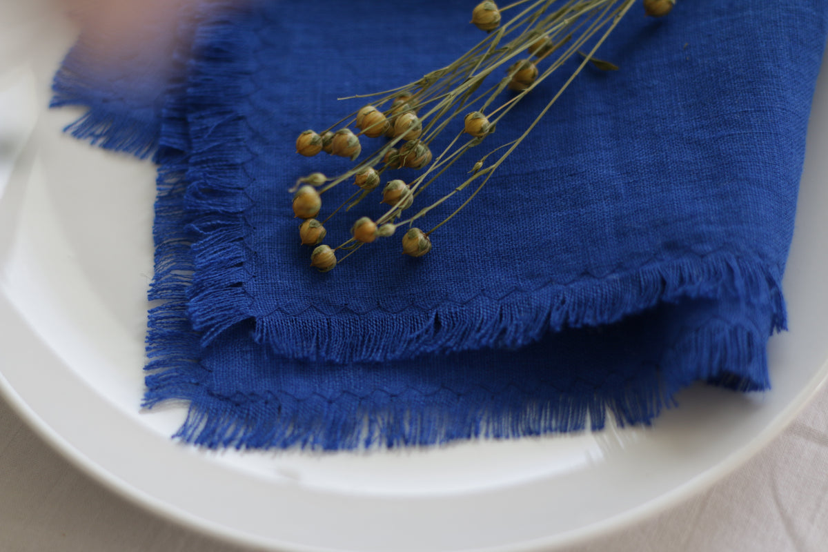 Cobald Blue linen napkin with frayed edges on a white plate with dried flowers.