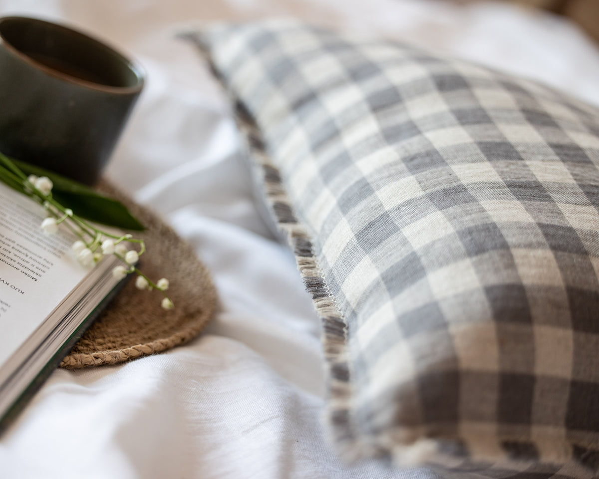Plaid linen pillow on a bed with an open book and mug