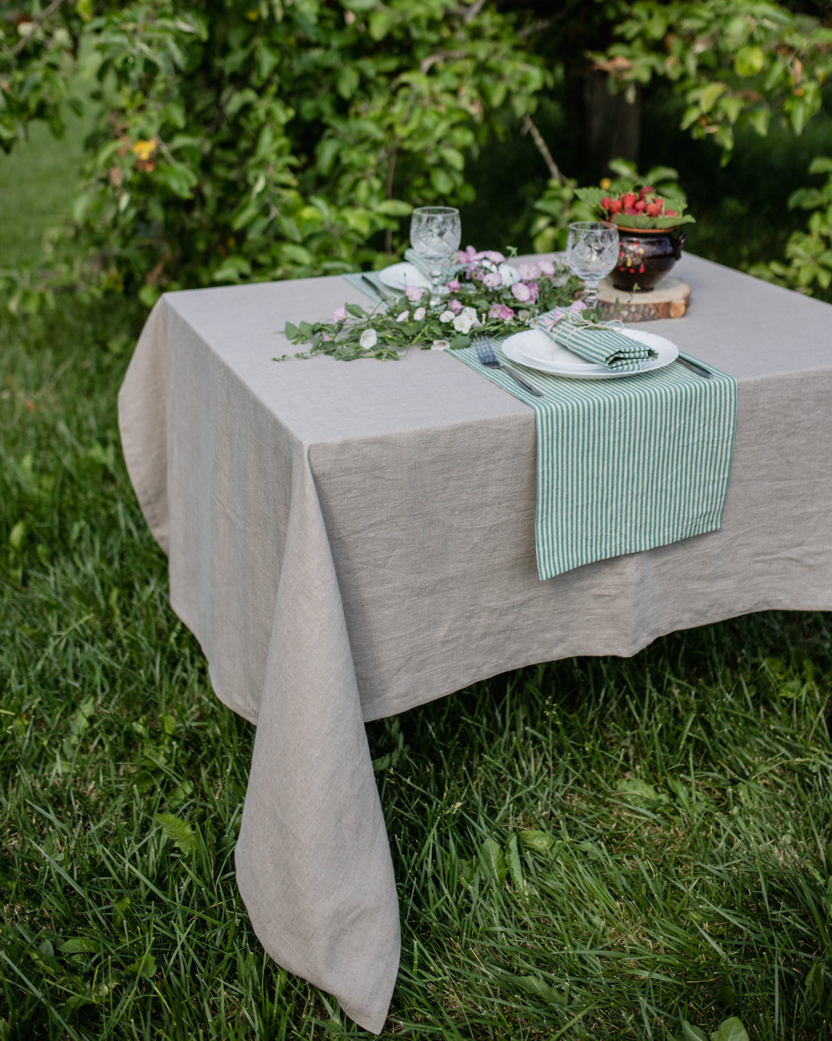 Table set for a meal outdoors with a gray tablecloth and green striped table runner