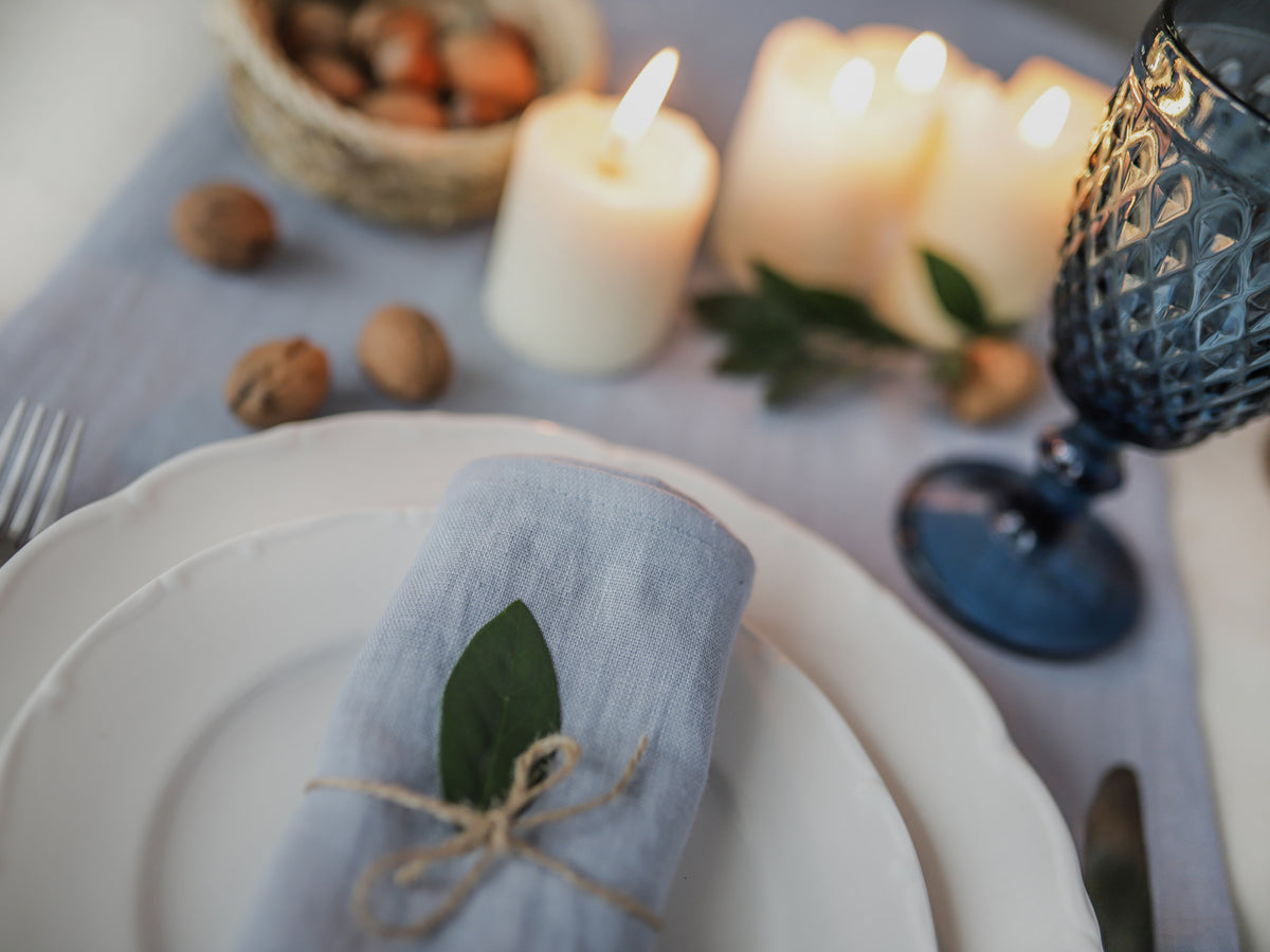 Set table with candles, dusty blue linen napkin, and silverware on a white surface