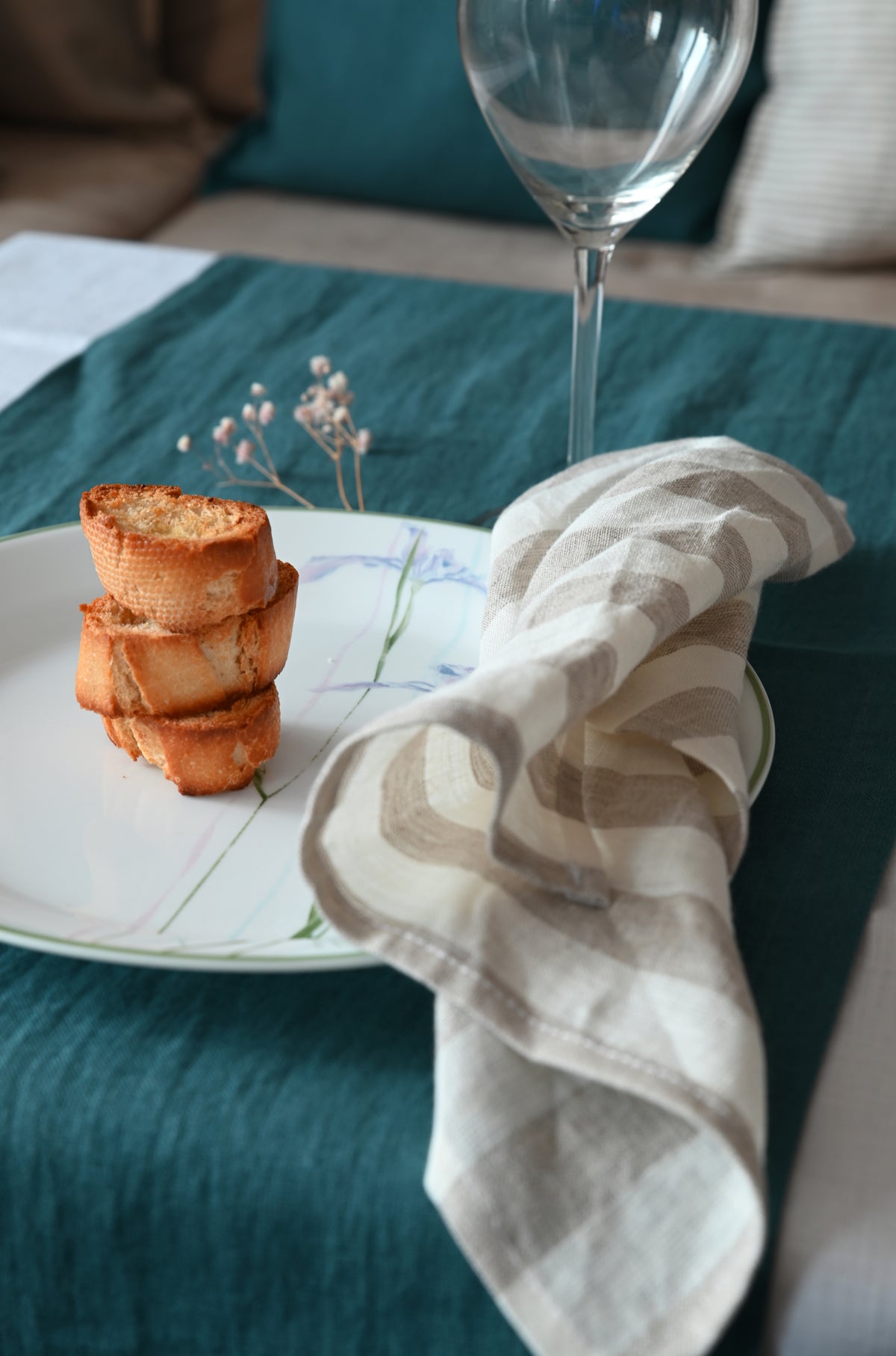 Small appetizer stack on a plate with a wine glass and striped linen napkin on a teal tablecloth.
