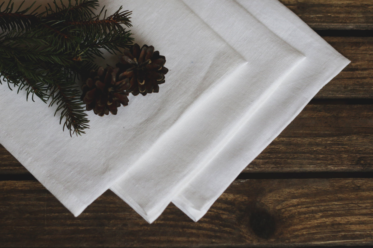 White linen napkins on a wooden surface with pine branches and cones.