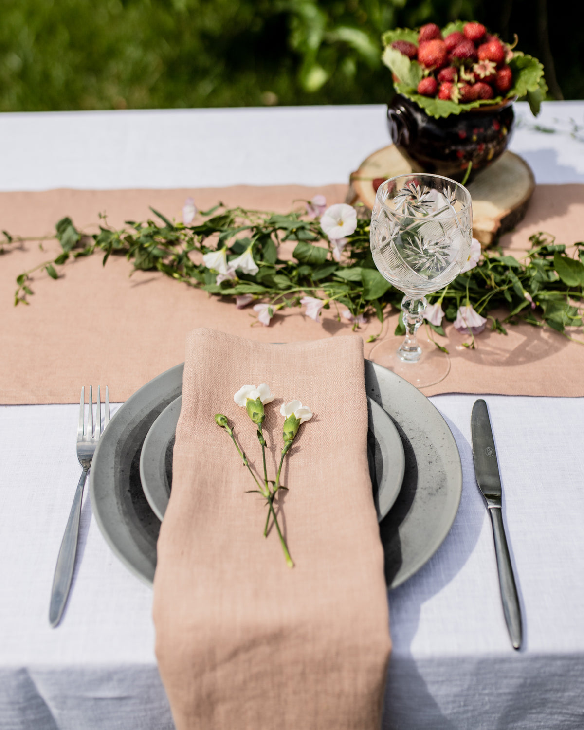 Elegant table setting with a beige napkin, greenery, and floral decorations.