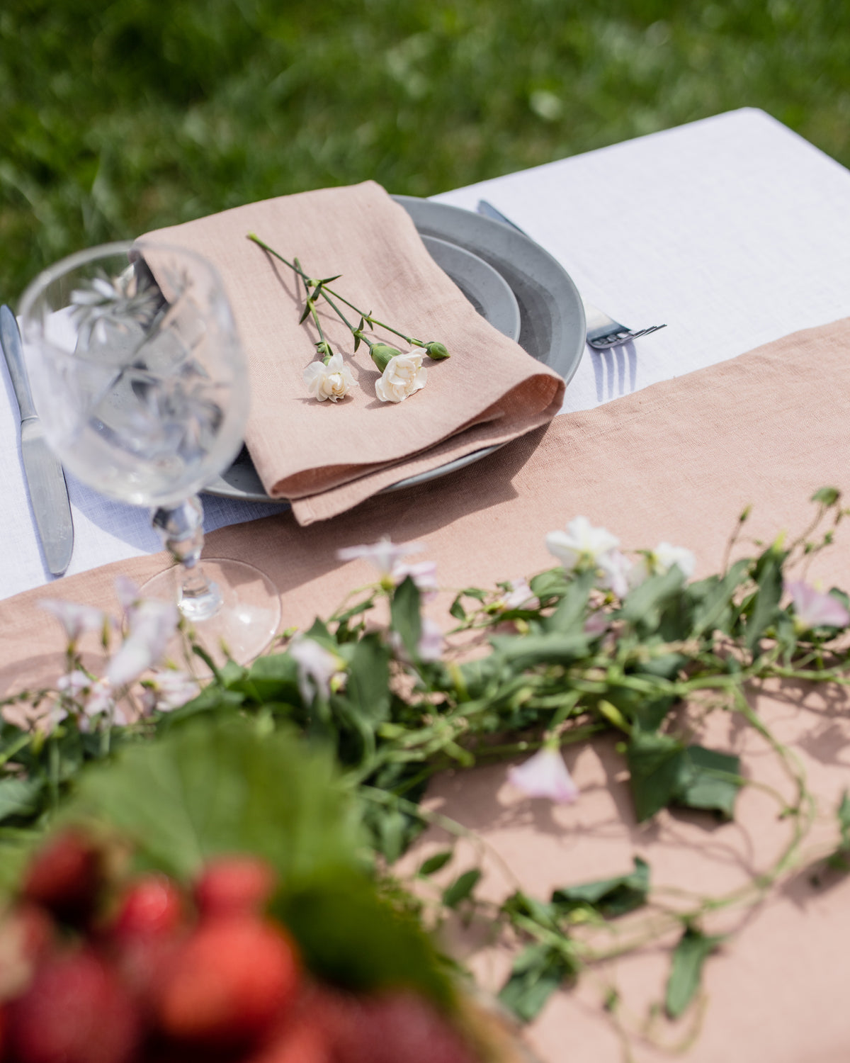 Table setting with a beige tablecloth, greenery, and white flowers on a grassy background