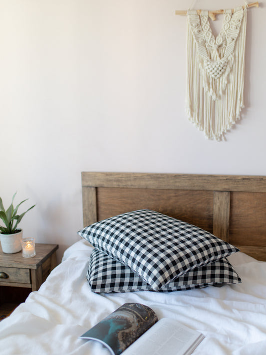 Bedroom with wooden headboard, checkered linen  pillow, and macrame wall hanging.