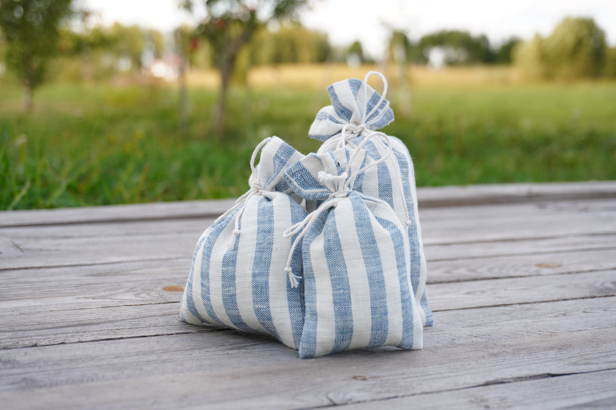 Two small striped pouches in blue and white  linen fabric sit on a weathered wooden deck with a blurred green outdoor background.