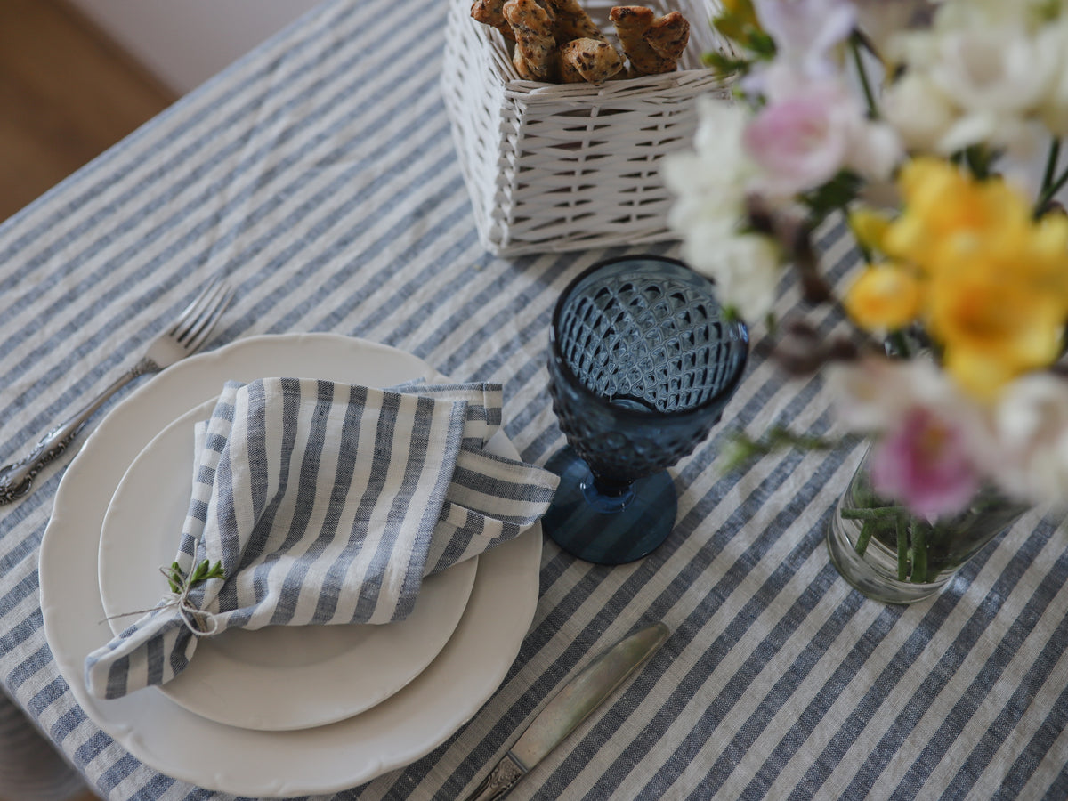 Dining table setting with striped tablecloth, plates, linen neutical striped napkin, and flowers.