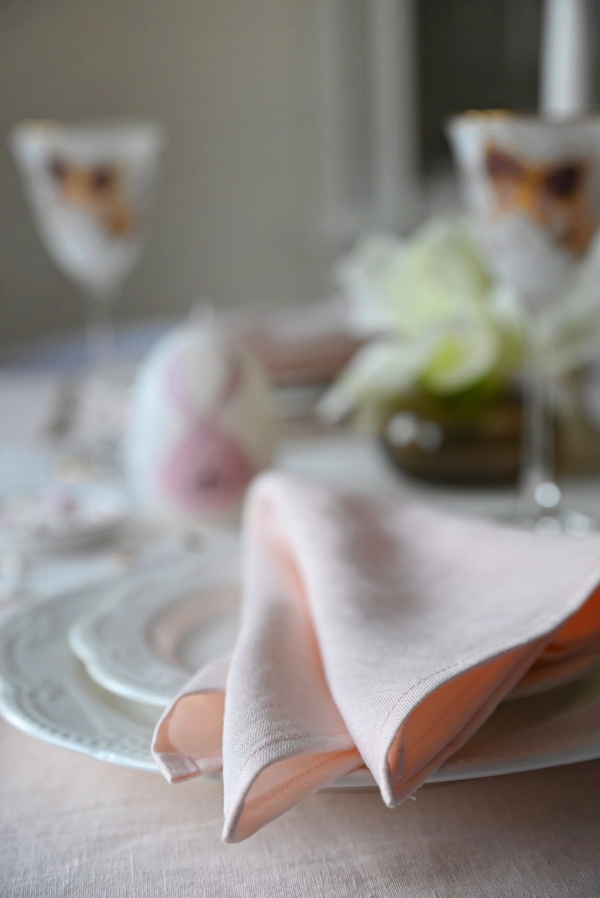 Table setting with blush pink napkin, plates, and glasses on a neutral background