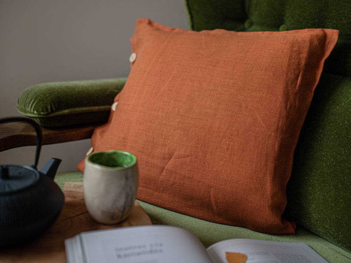 Orange pillow on a green couch with a teacup and book nearby