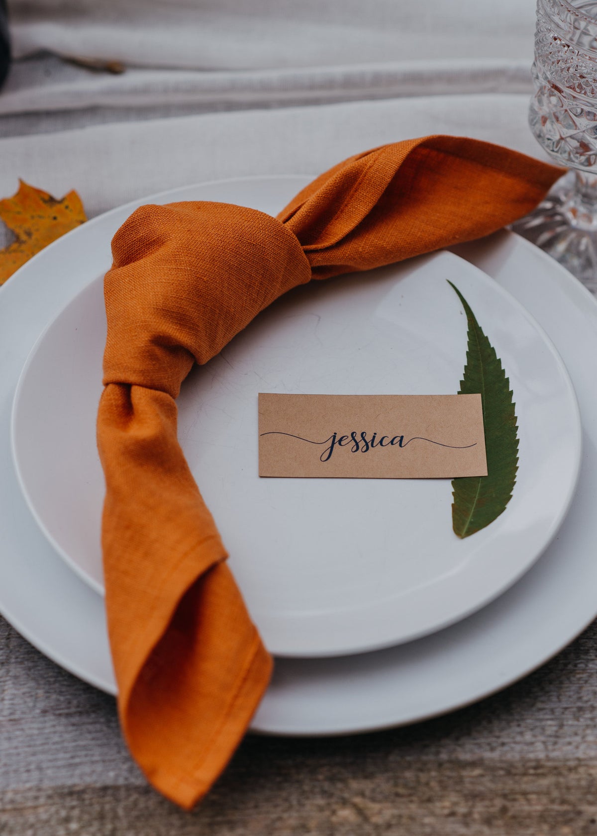 Place setting with orange linen  napkin, name card, and leaf on a white plate.