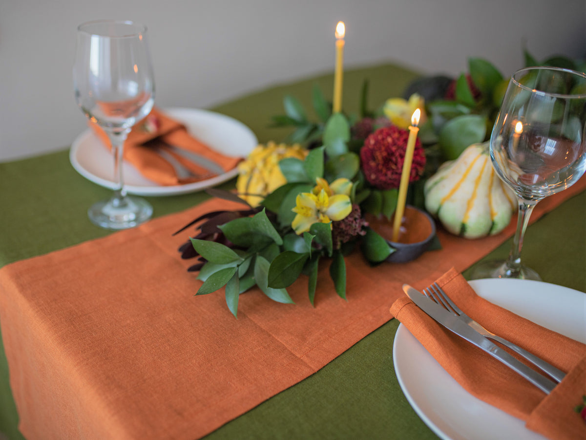 Set table with orange napkins, green leaves, and candles on a green tablecloth.