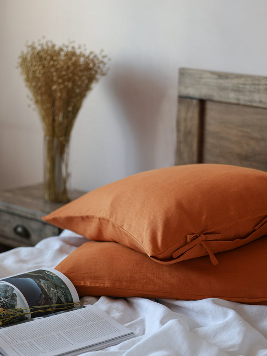 Orange pillows on a bed with a book and vase in the background