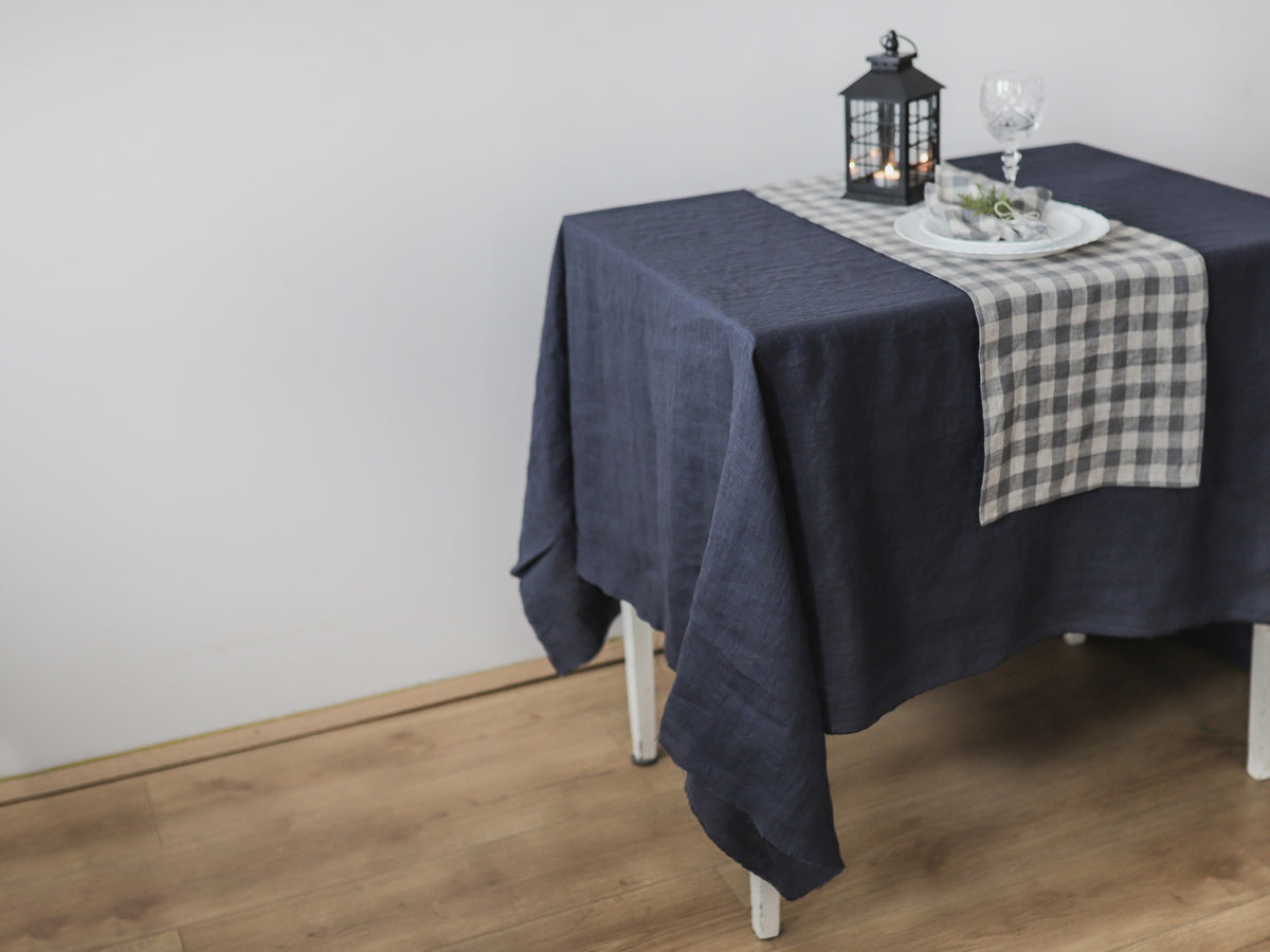 Dark gray linen  tablecloth on a wooden table with a checkered runner and candle lantern.