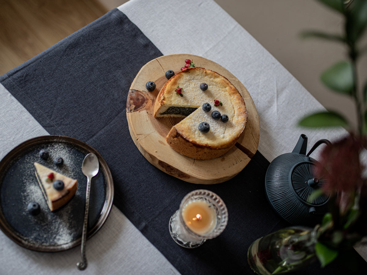 Pie with a slice removed on a wooden board, surrounded by a teapot, candle, and dessert plate.