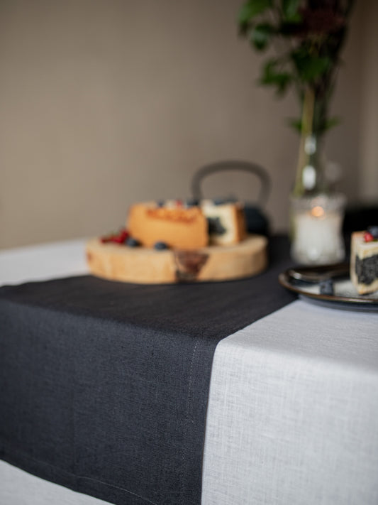 Table setting with a dark gray table runner, wooden board with food.