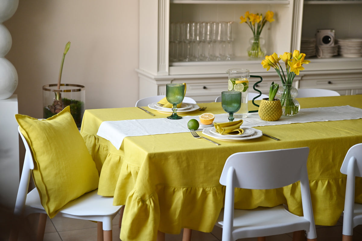 Dining table set with chartreuse  linen tablecloth, green glasses, and white chairs in a kitchen.