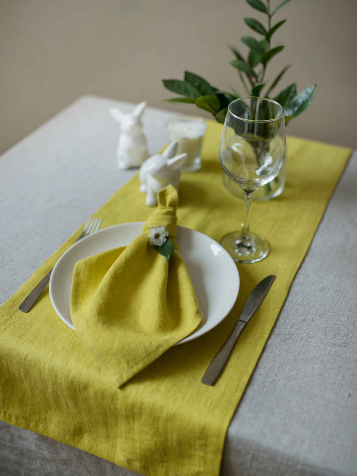 Table setting with a chartreuse napkin, white plate, and glass on a gray tablecloth.