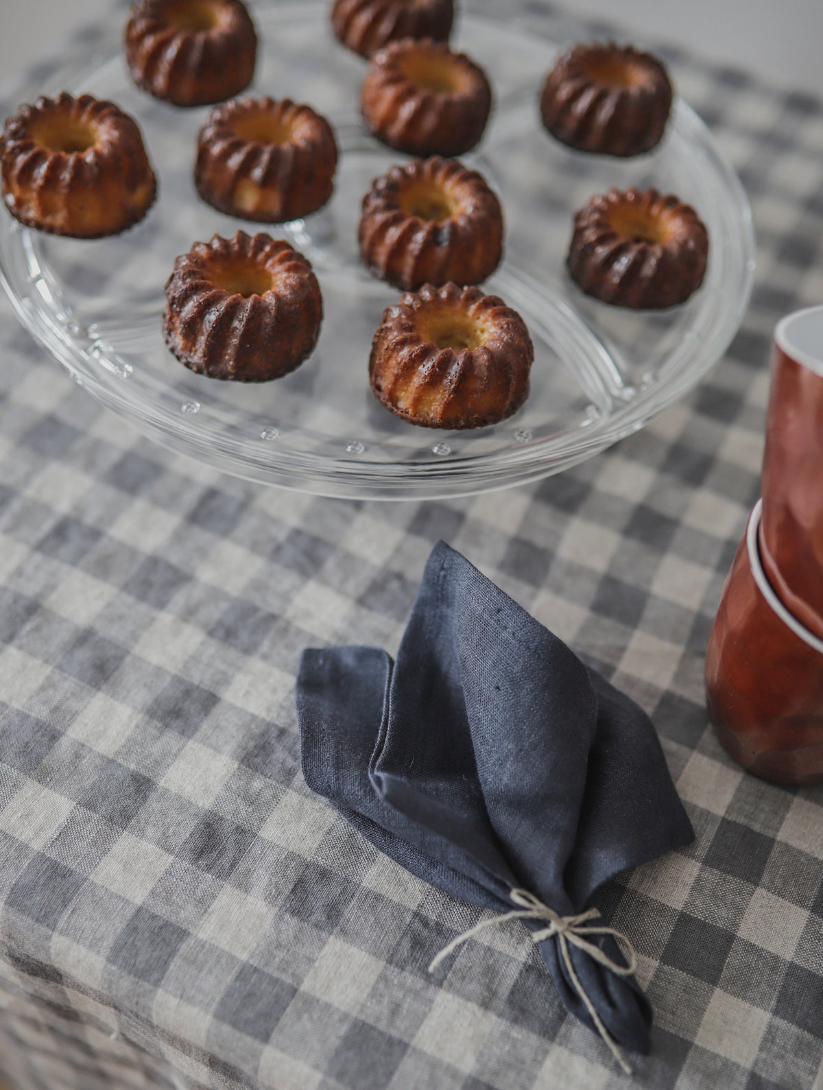 Small round baked goods on a clear glass plate with a checkered linen tablecloth and red cup in the background.