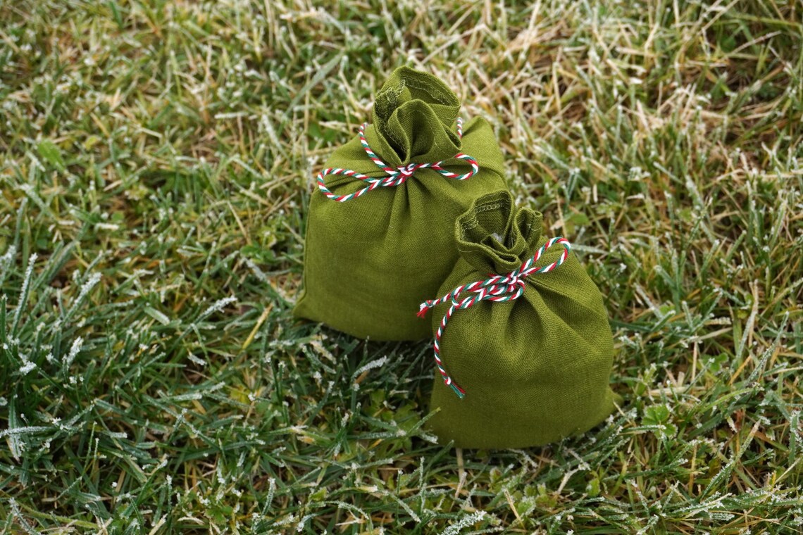 Two olive green fabric pouches tied with red, white, and blue braid, placed on a frosty green grass lawn.