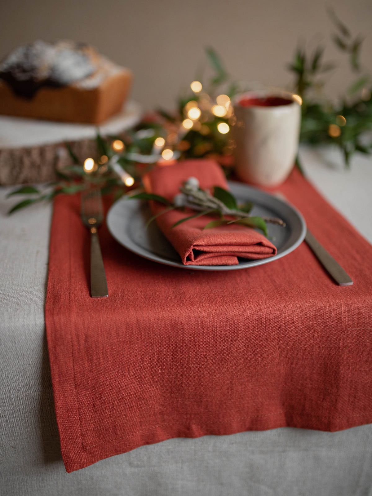 Set table with clay linen napkins , white plates, and silverware on a wooden table.
