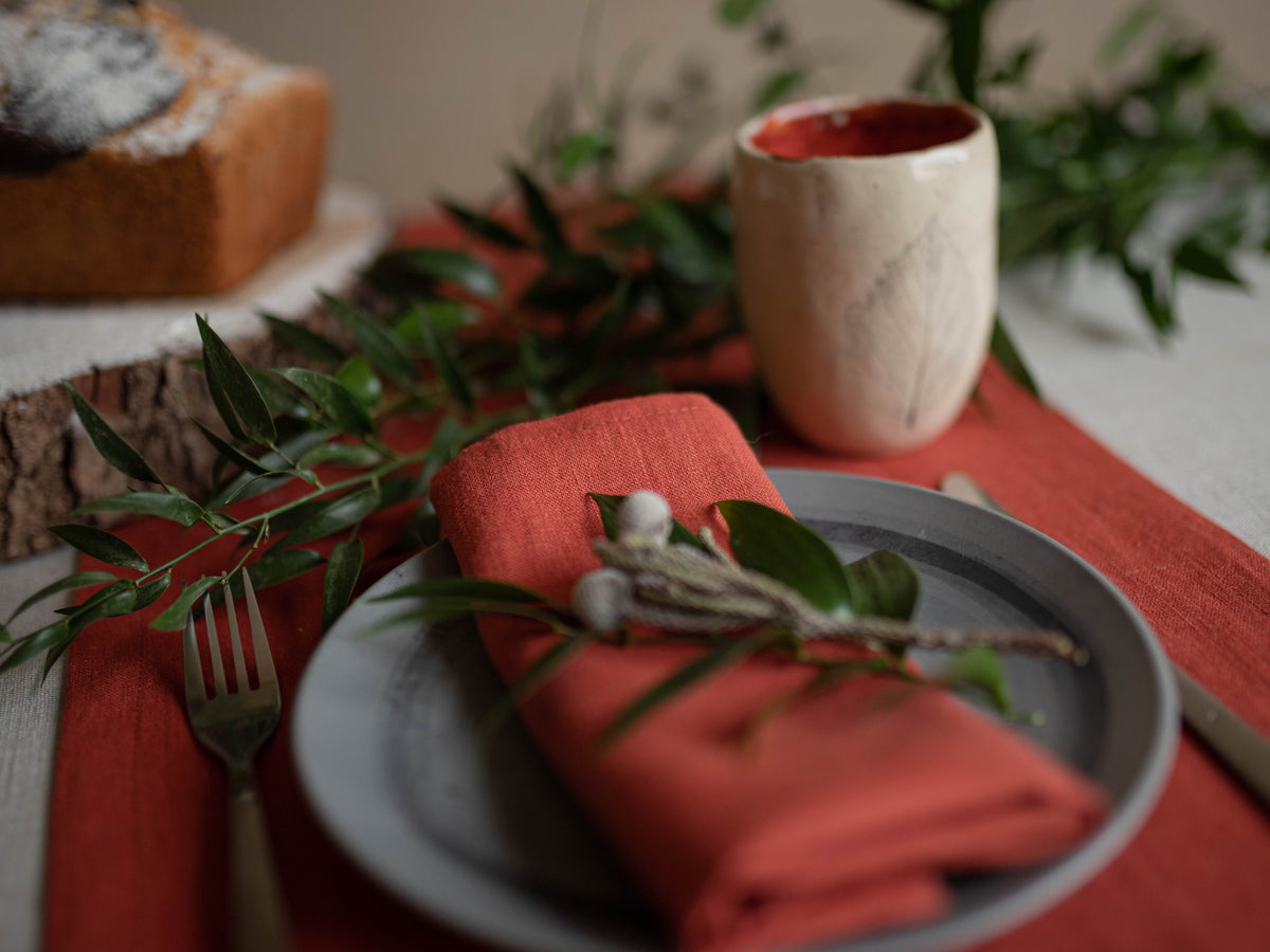 Table setting with clay terracotta napkin, greenery, and a cup on a clay table runner.