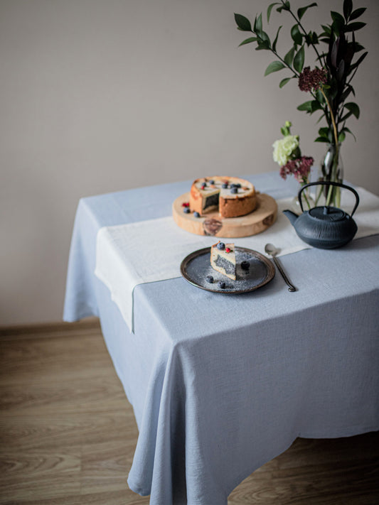 Table setting with a dusty blue linen  tablecloth, cake, and teapot.