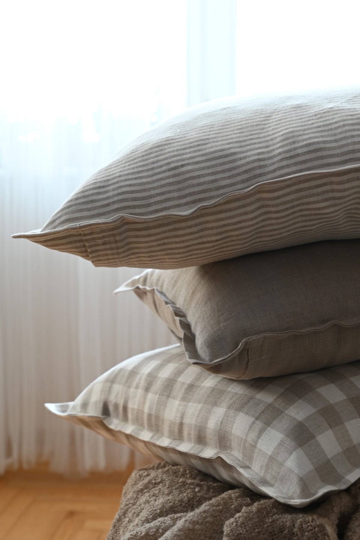 Stack of linen pillows with striped and checkered patterns on a neutral background