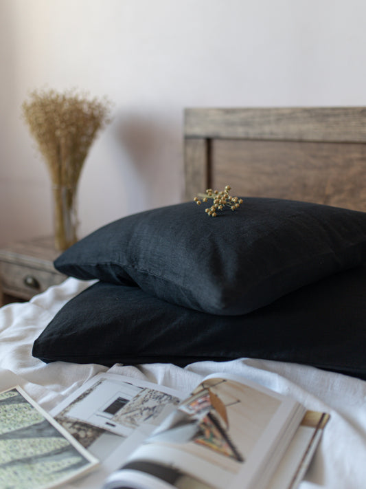 Black linen  pillows on a bed with a wooden headboard and decorative items.