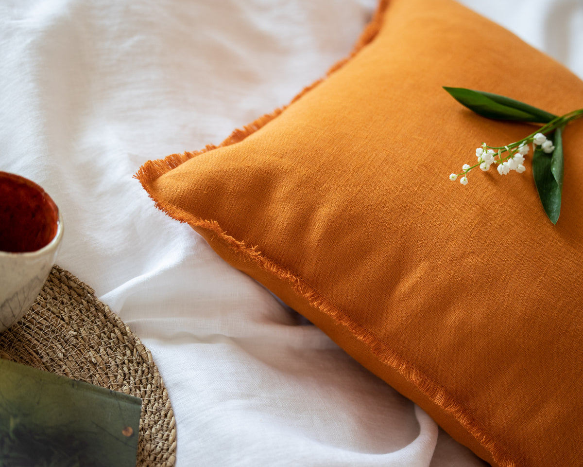 Orange pillow with a sprig of flowers on a white linen bedding