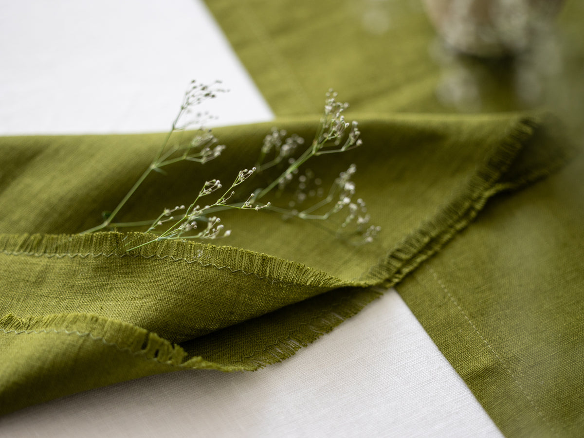 Olive Green fringed linen napkin with a branch of small flowers on a white surface