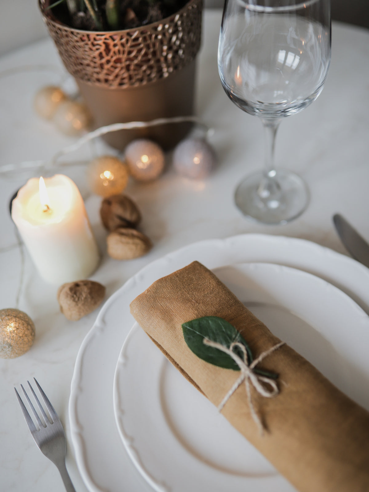 Table setting with a golden brown linen napkin, candle, and wine glass on a white surface.