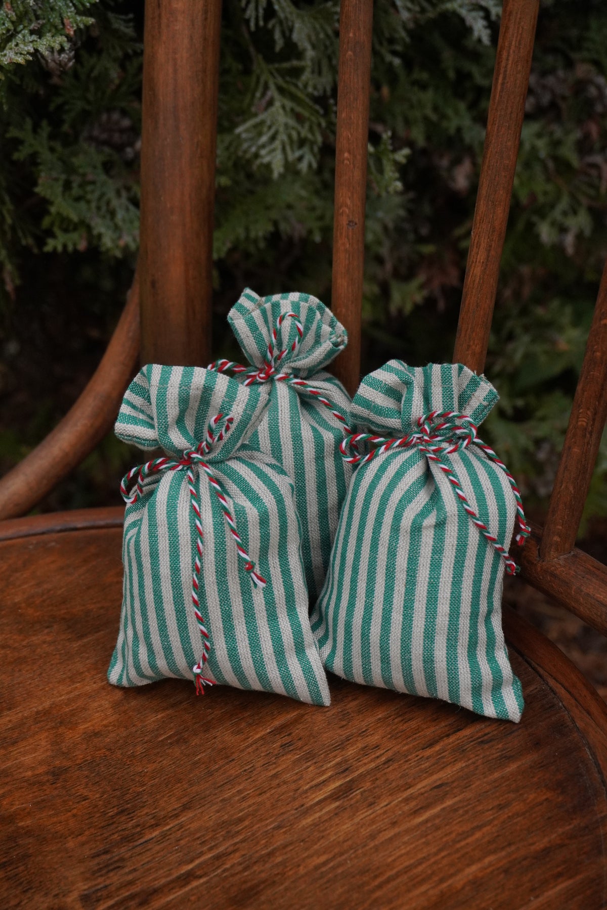Two small drawstring gift bags with green and white vertical stripes sit on a wooden chair outdoors