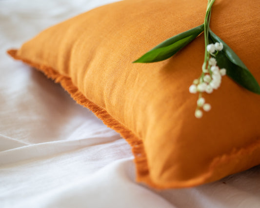 Orange pillow with a sprig of white flowers on a white background