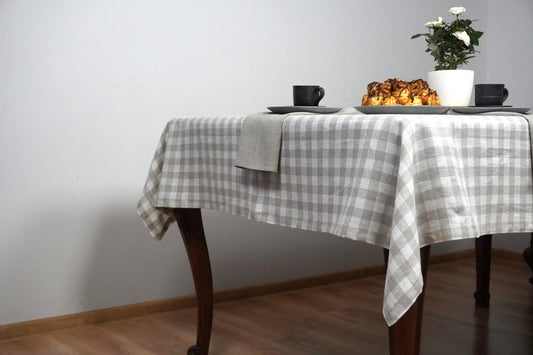Round table with a checkered tablecloth, a cup, a plate, and a small plant against a white wall.