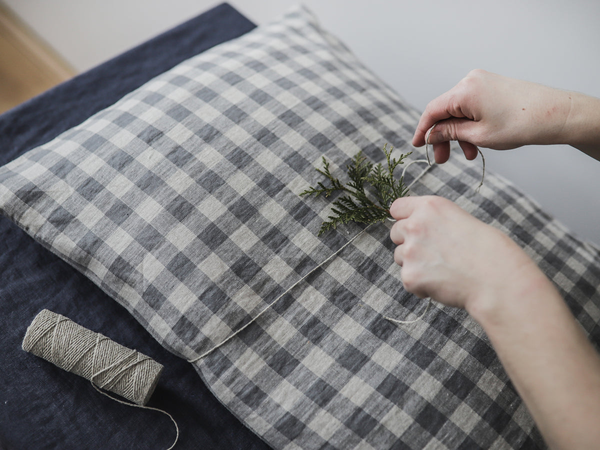Person arranging a branch on a checkered fabric linen pillow cover with a spool of thread nearby.