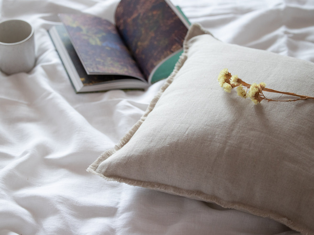 Book and mug on a bed with a pillow and dried flowers
