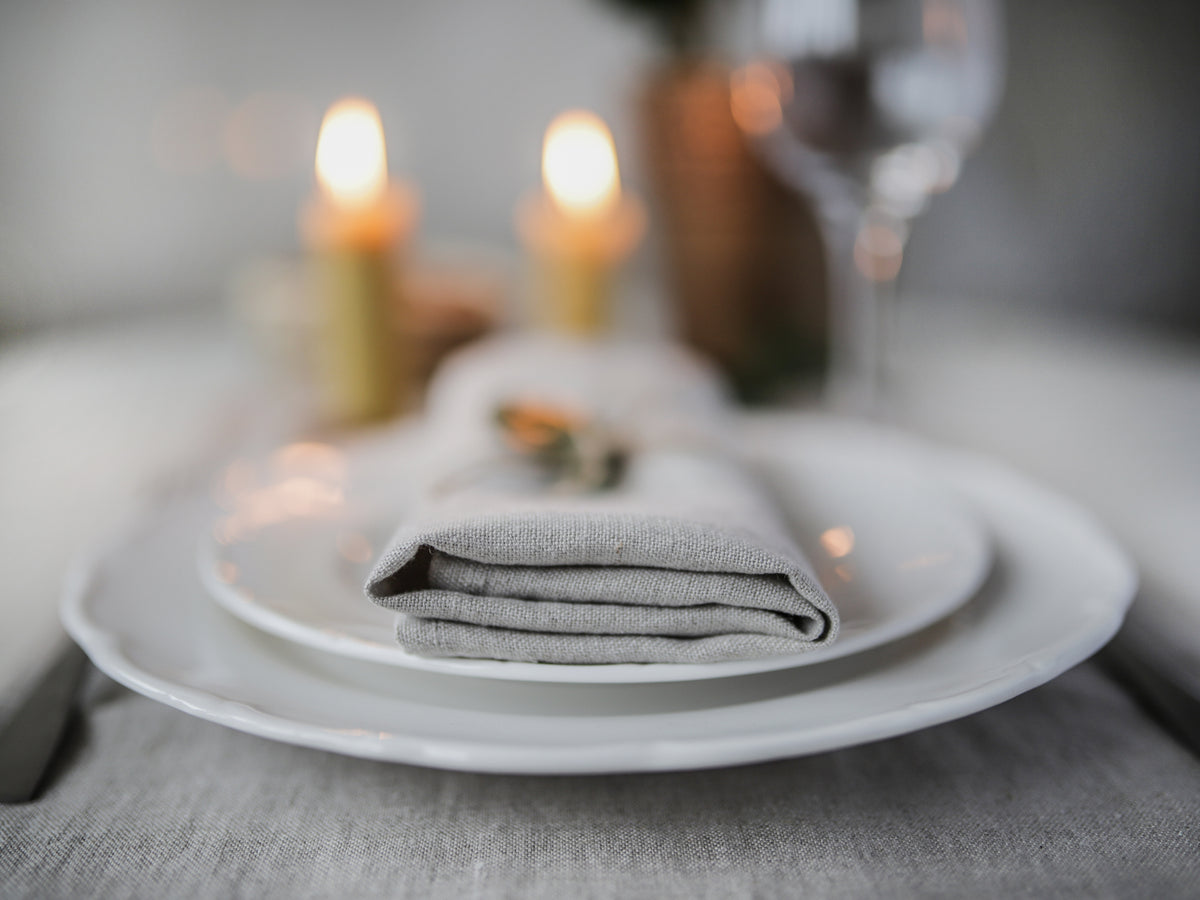 Folded gray napkin on a white plate with blurred candles and wine glasses in the background