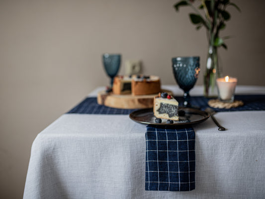 Dining table setting with a slice of cake, glasses, navy blue checkered linen napkin  and a candle.