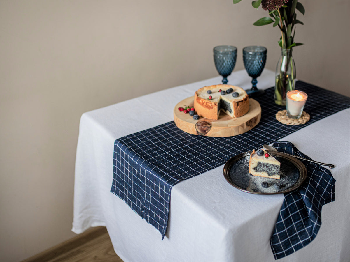 Table setting with a cheese platter and dessert on a white tablecloth with a blue checkered runner.