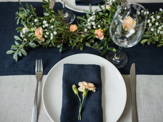 Elegant table setting with white plates, navy linen  napkins, and floral decorations on a dark blue tablecloth.