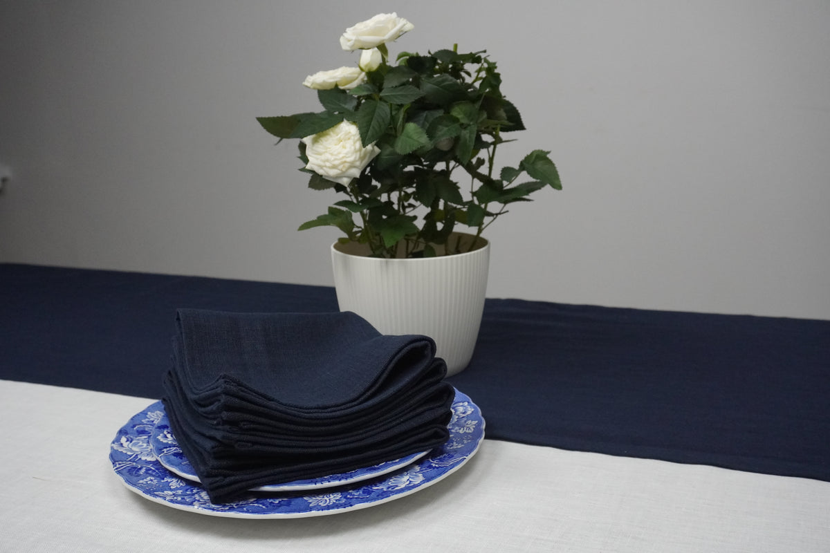 Navy blue linen  napkins on a blue and white patterned plate with a potted plant on a gray background