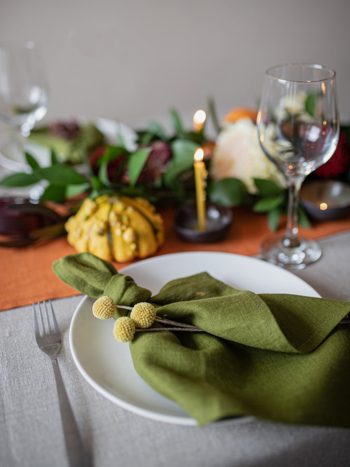 Table setting with olive green linen napkin, candle, and autumn decorations.