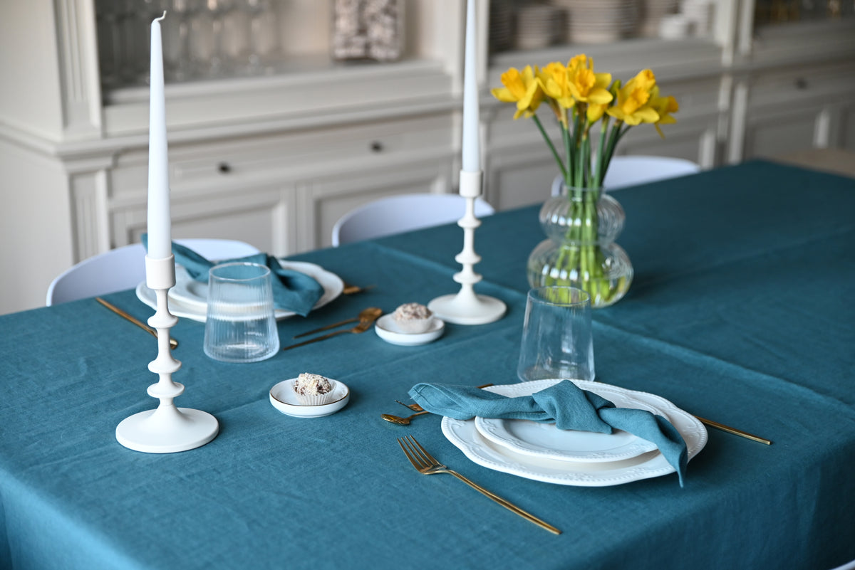 Elegant table setting with patina blue tablecloth, white plates, gold cutlery, and yellow flowers.