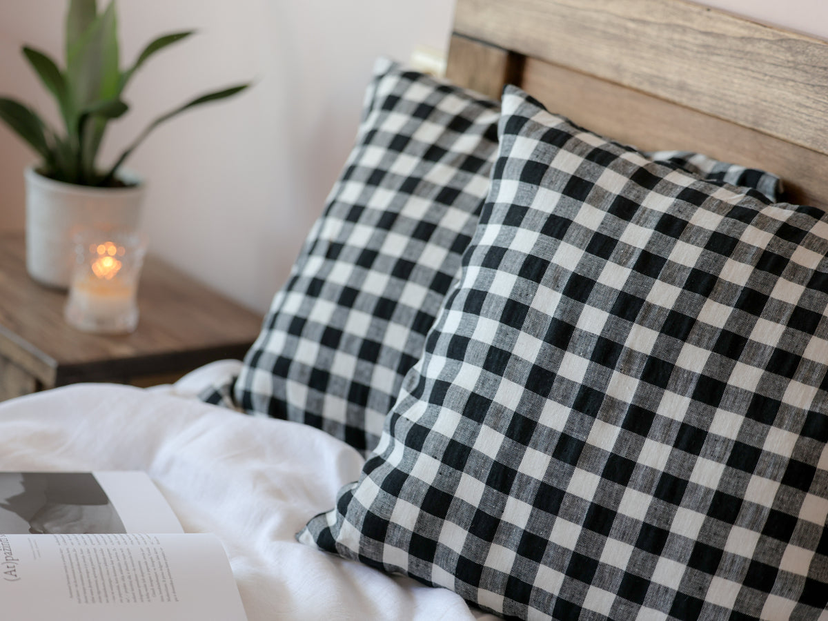 Black and white checkered pillows on a bed with a candle and plant in the background.