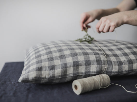A girl  arranging dried herbs on a plaid linen pillow with a roll of yarn beside it.