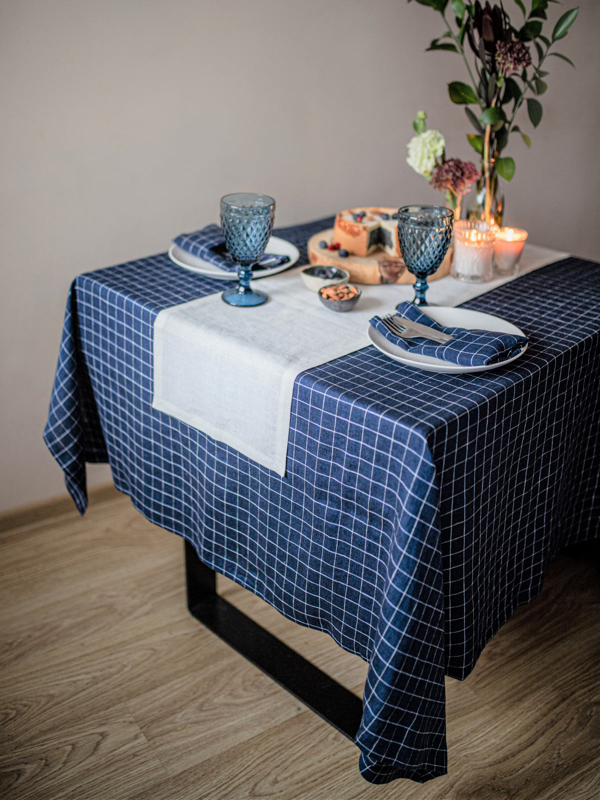 Dining table set with a blue checkered tablecloth, plates, glasses, and a centerpiece.