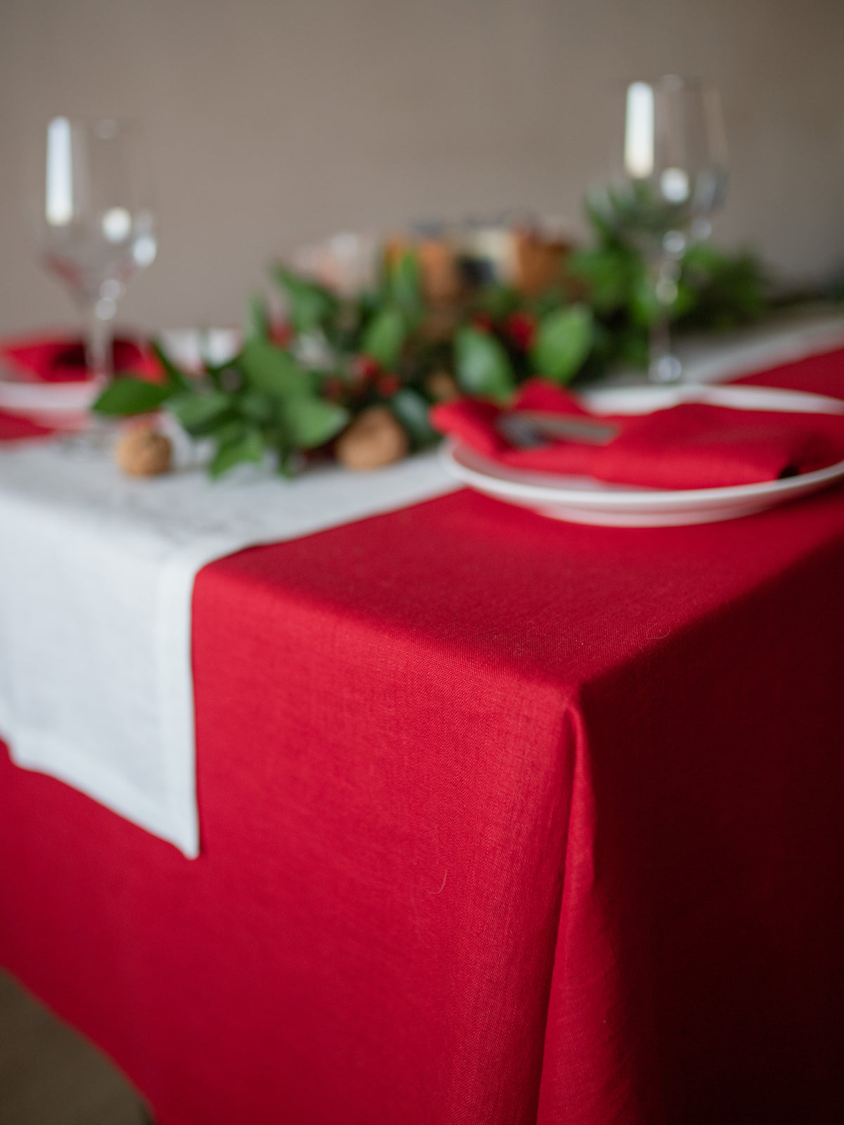 Decorative table setting with white runner, red linen tablecloth, and greenery.