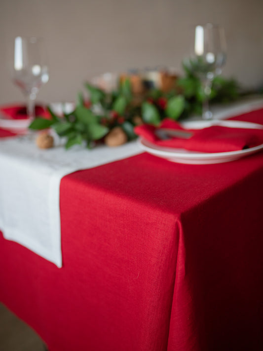 Decorative table setting with white runner, red linen tablecloth, and greenery.
