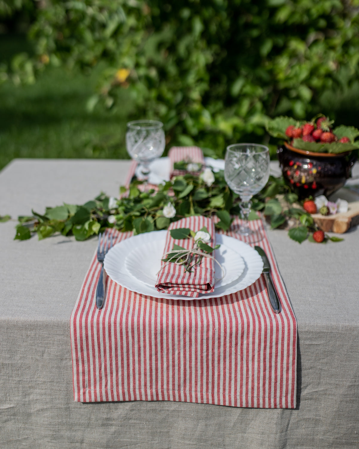 Outdoor table setting with a red and white checkered table runner, white plates, and greenery.