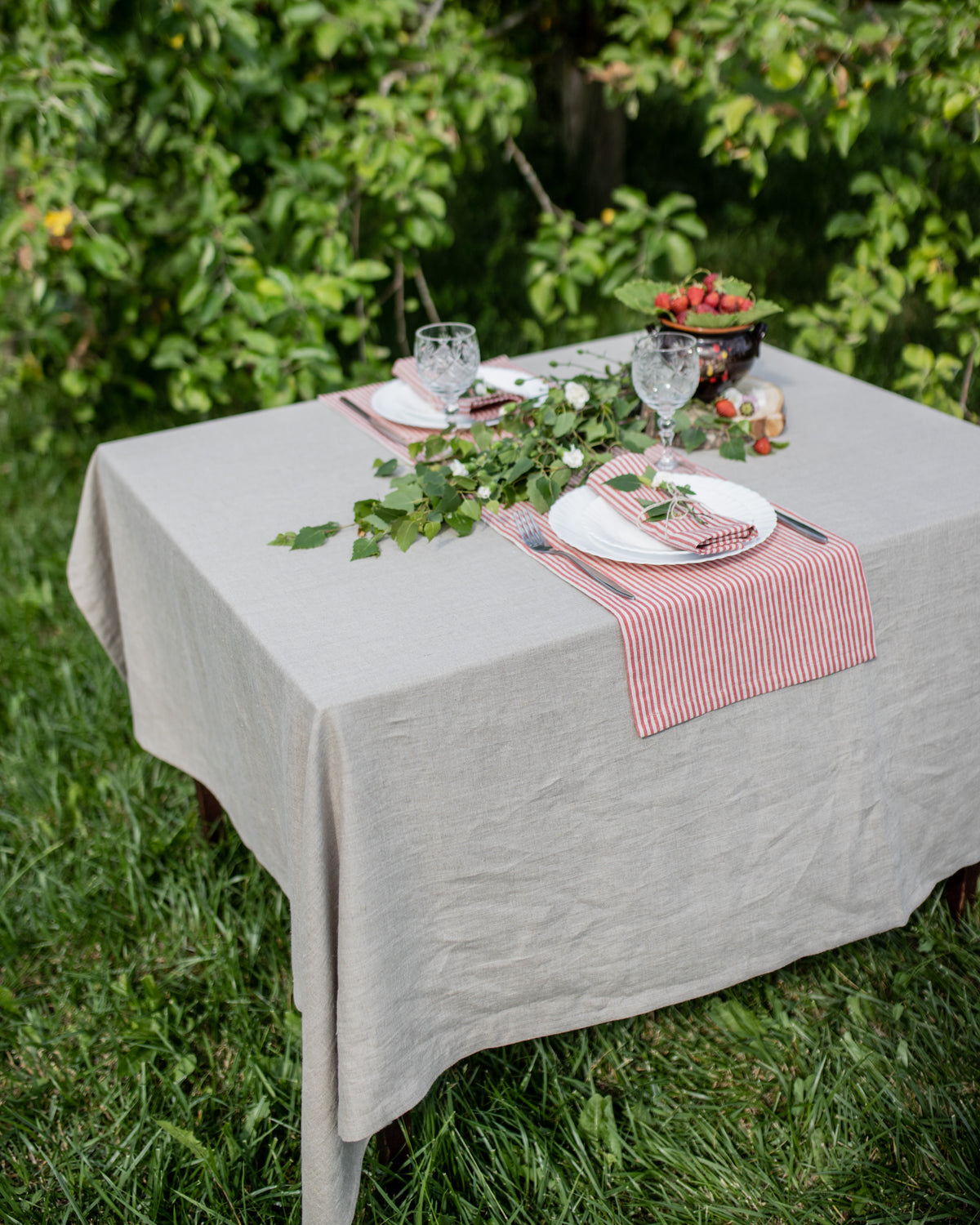 Table set for a meal outdoors with a green tablecloth, red and white striped napkins, and glasses.